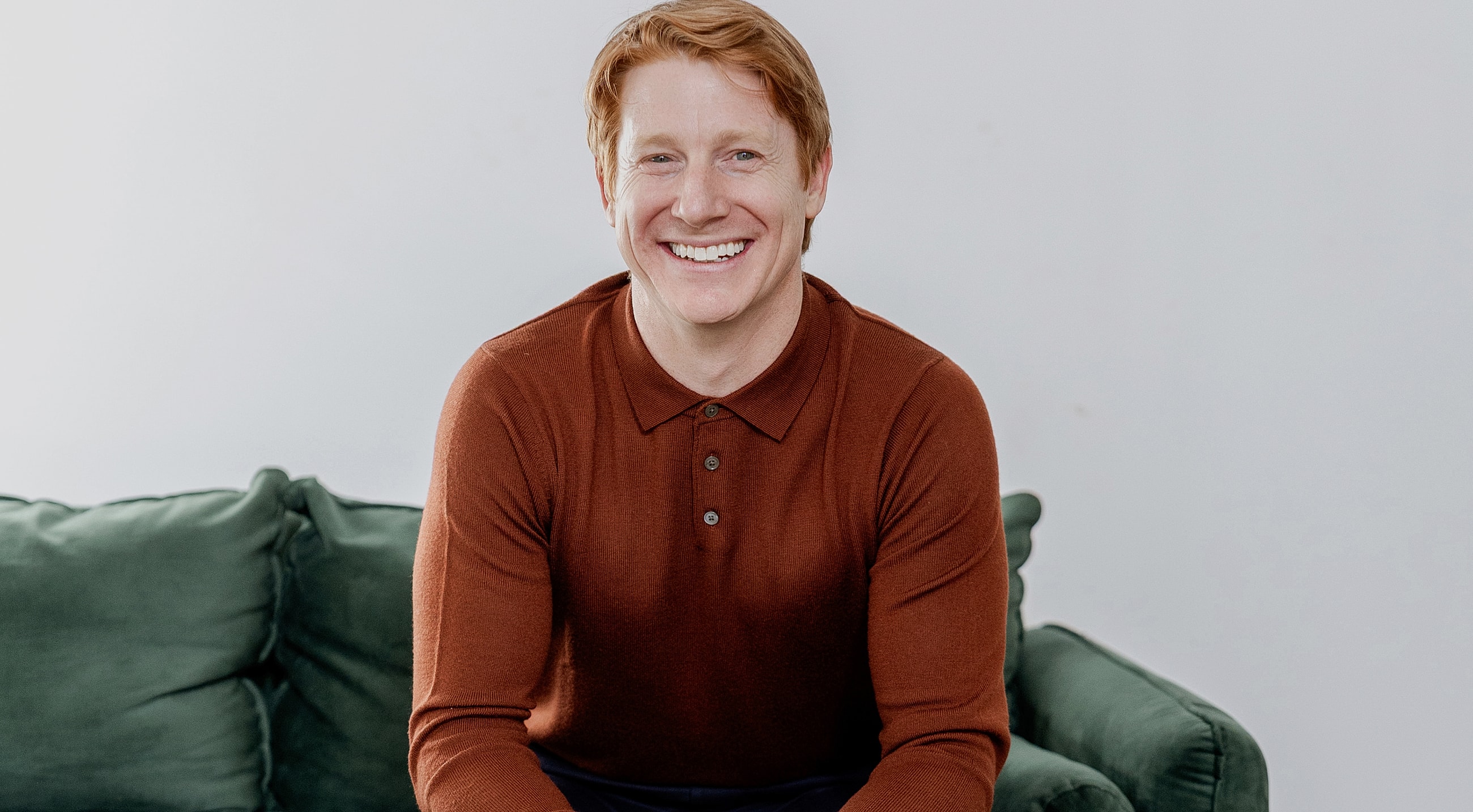 Smiling man sitting on a green couch.